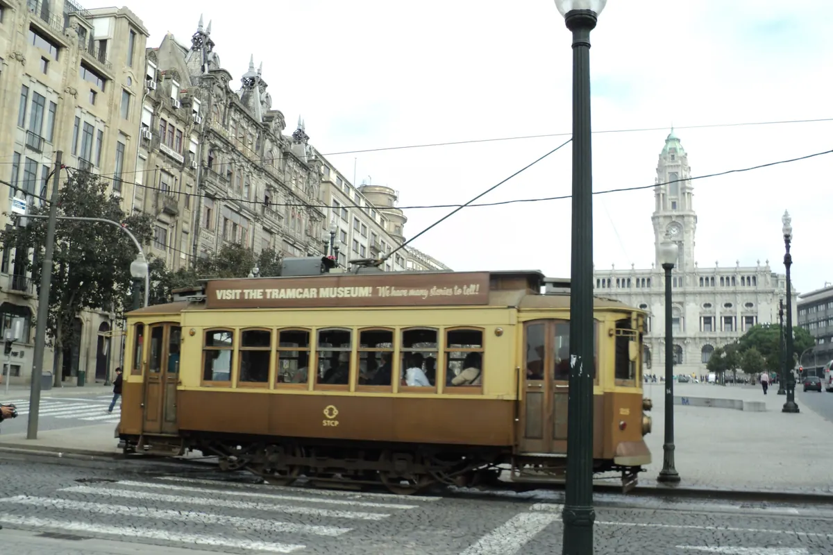 A vintage tram on a wide Porto avenue, with the City Hall tower behind it